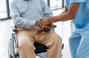 older man in a wheel chair holding the hand of a nurse