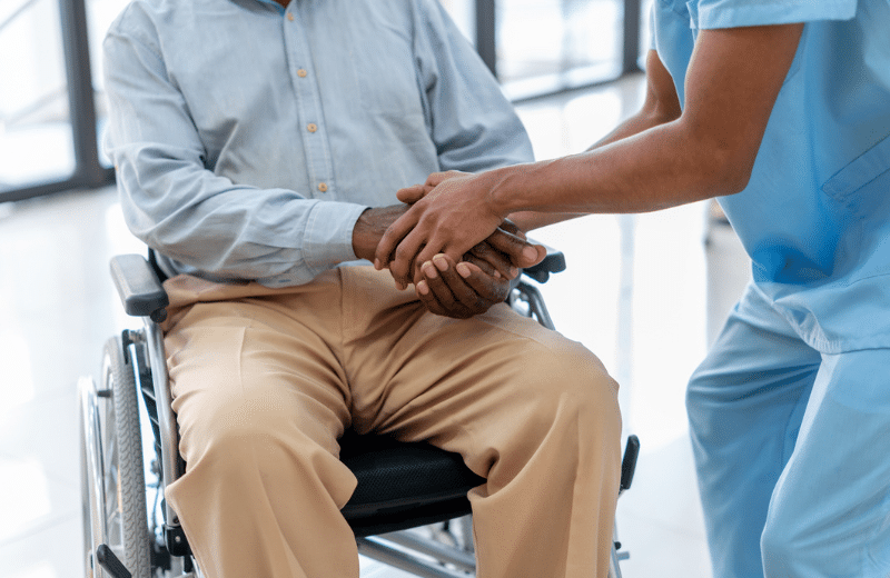 older man in a wheel chair holding the hand of a nurse