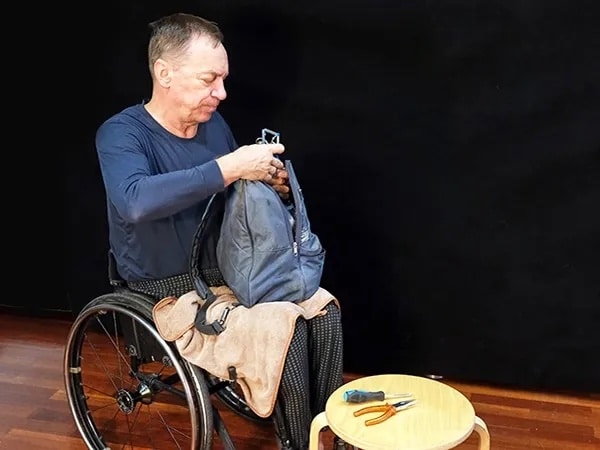 Man in wheelchair prepares backpack with emergency supplies